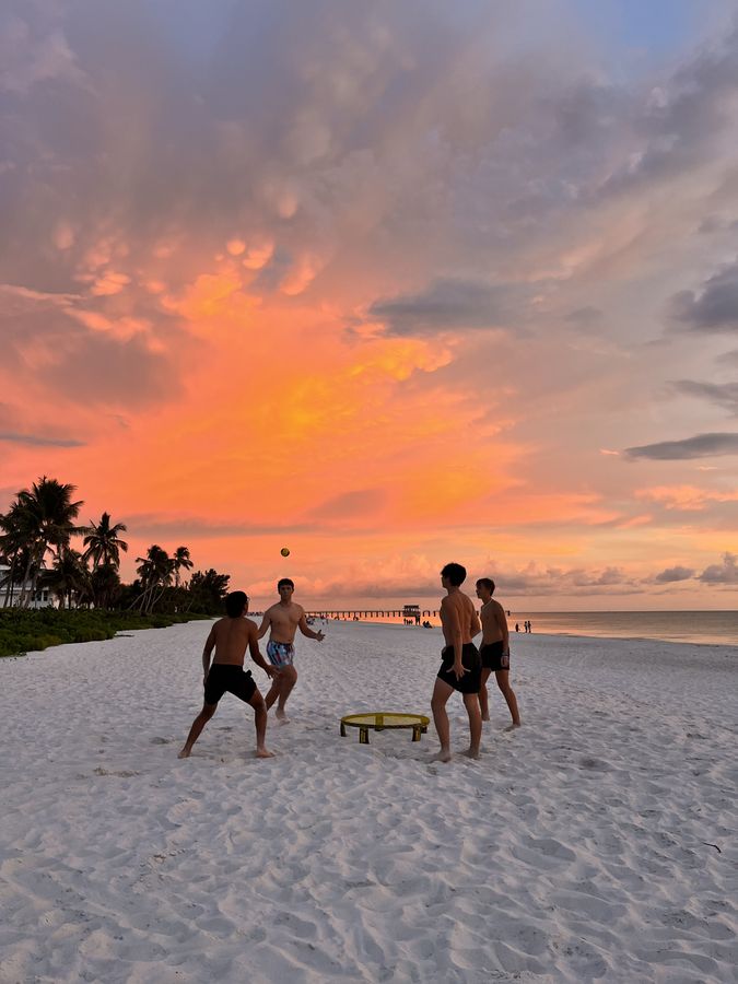 Friends playing spikeball on the beach under a burning sunset
